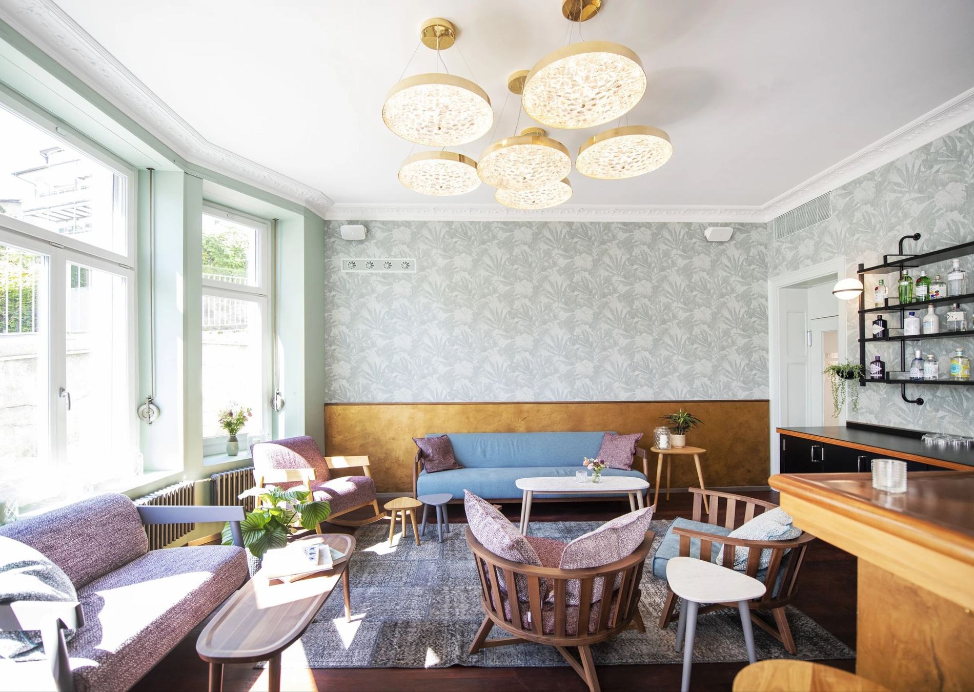 Die Lounge des Alma mit goldenen Leuchten, Palmentapete und Sesseln